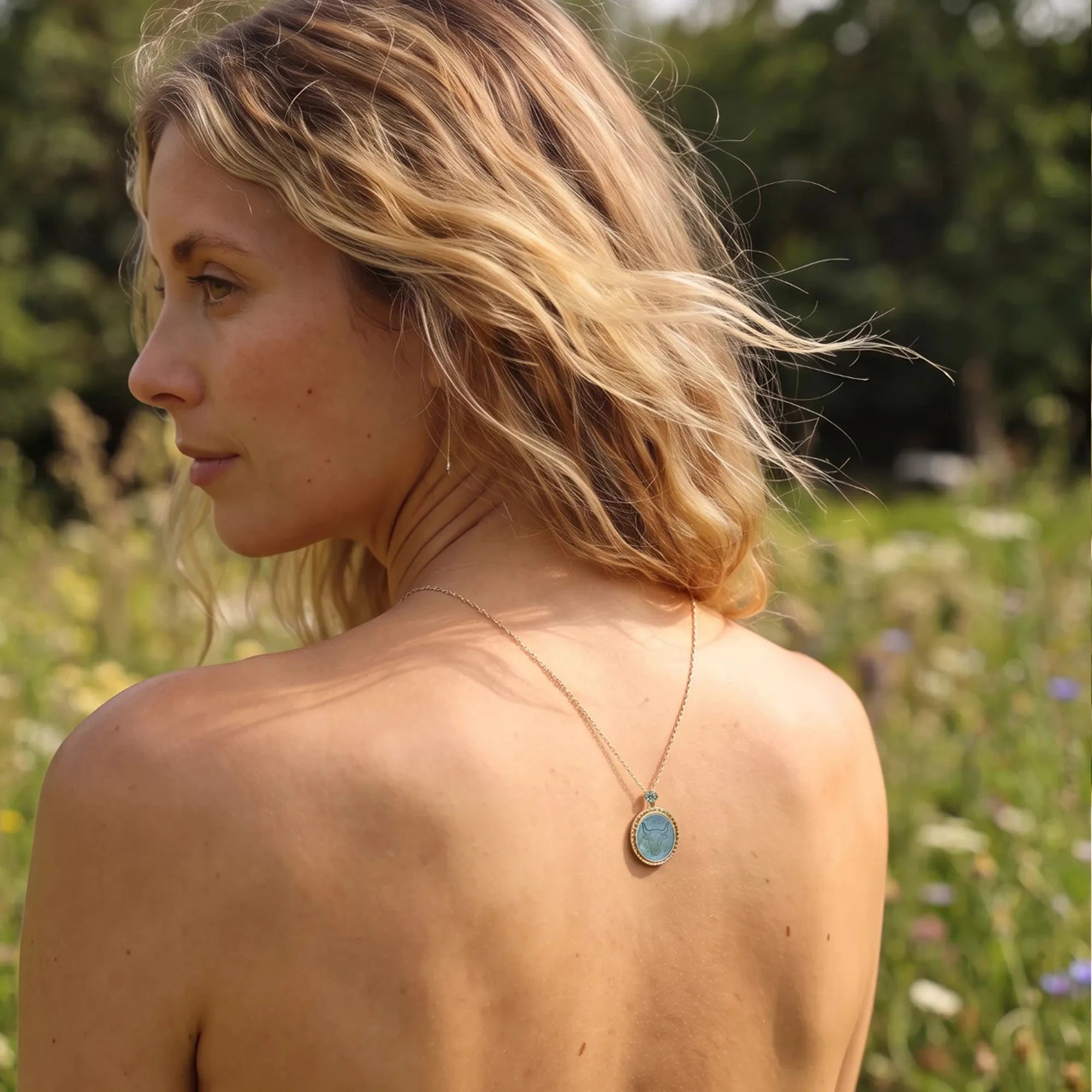 Model standing in a flower field, side profile, wearing an Archaeological Style Taurus zodiac sterling silver gold-plated pendant necklace by OceanCarvingLab，