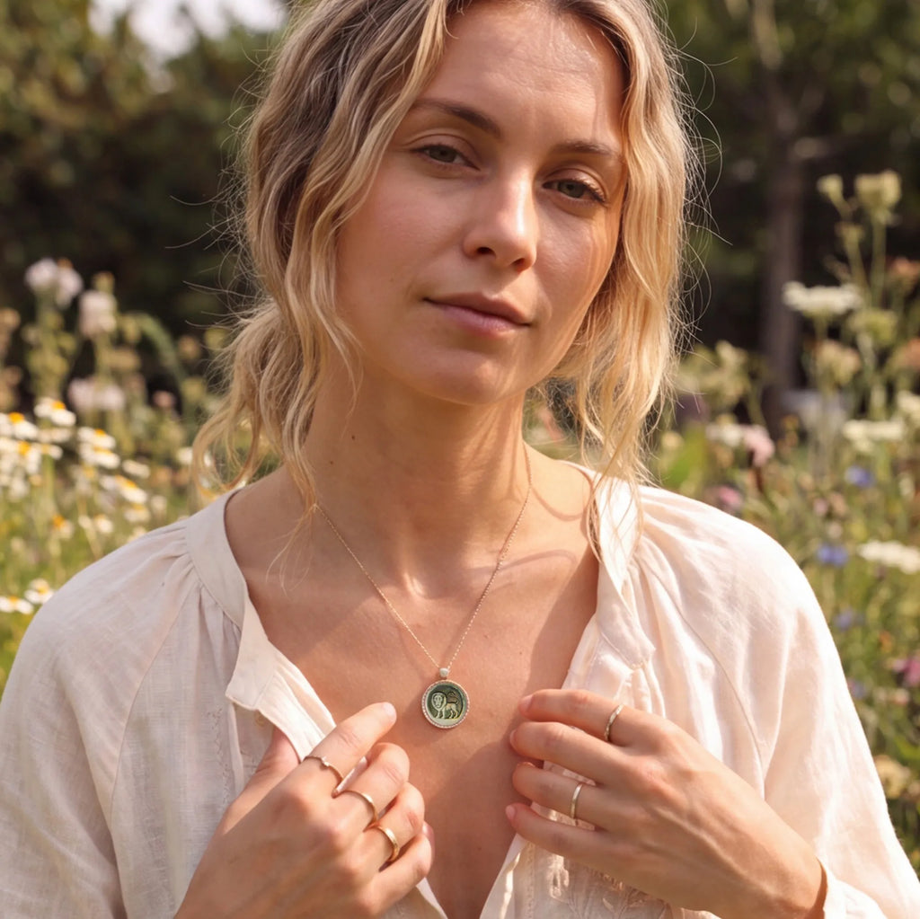 Elegant blonde woman among wildflowers in the countryside while wearing a Picasso‑inspired abstract  Leo zodiac pendant necklace with natural mother‑of‑pearl carving by OceanCarvingLab.