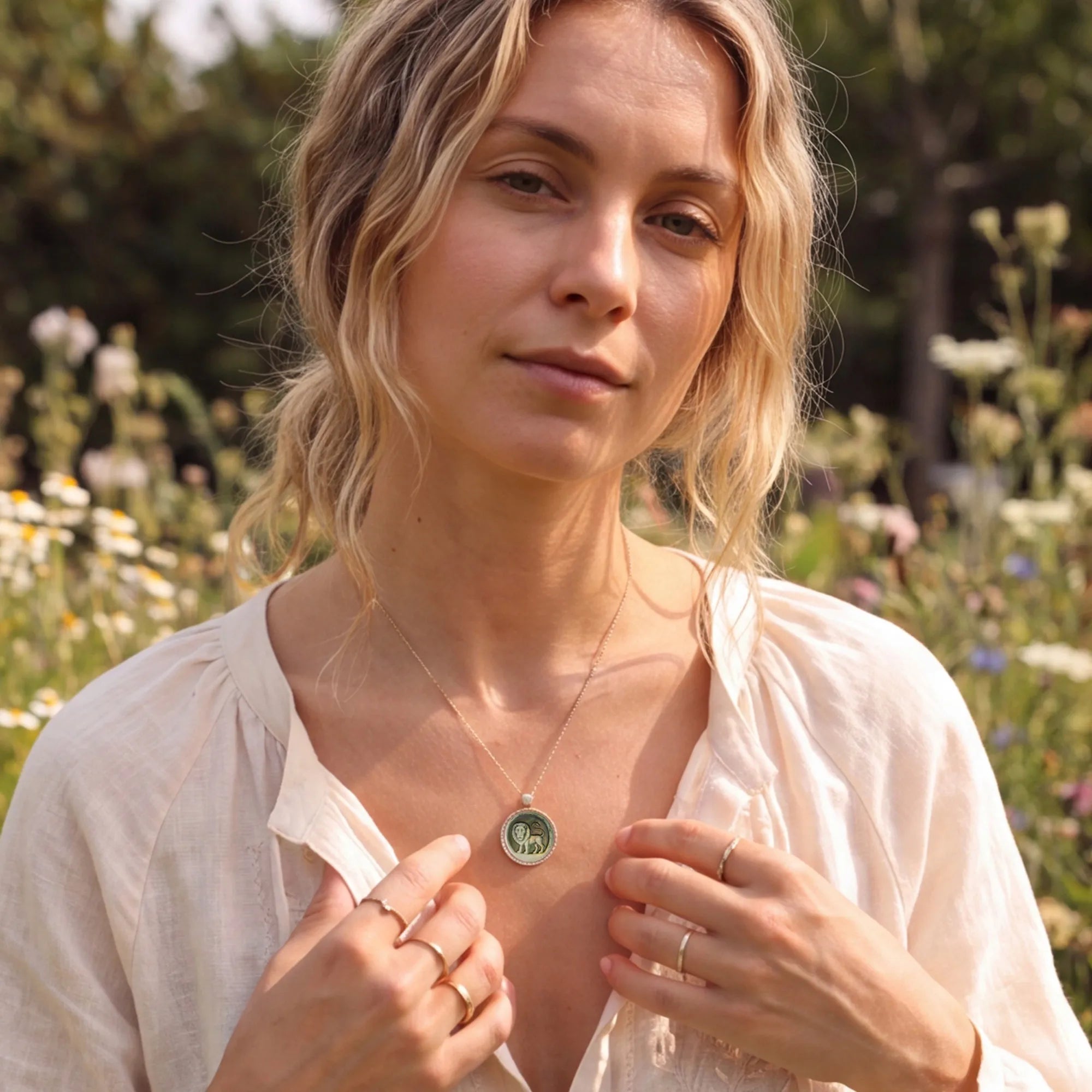 Elegant blonde woman reading outdoors while wearing a Picasso-inspired abstract zodiac pendant necklace with natural mother-of-pearl carving by OceanCarvingLab.