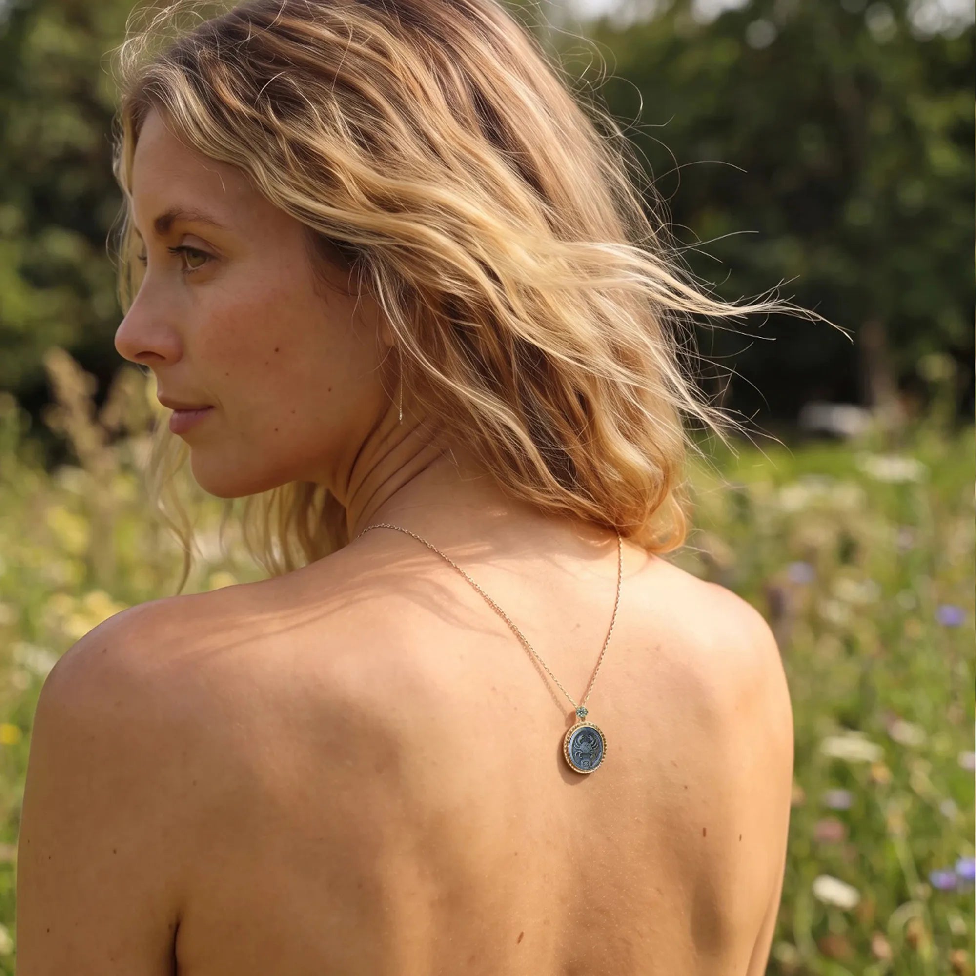 Elegant blonde woman amid countryside wildflowers wearing a Van Gogh style carved  Cancer zodiac mother‑of‑pearl pendant necklace in gold plated sterling silver by OceanCarvingLab.