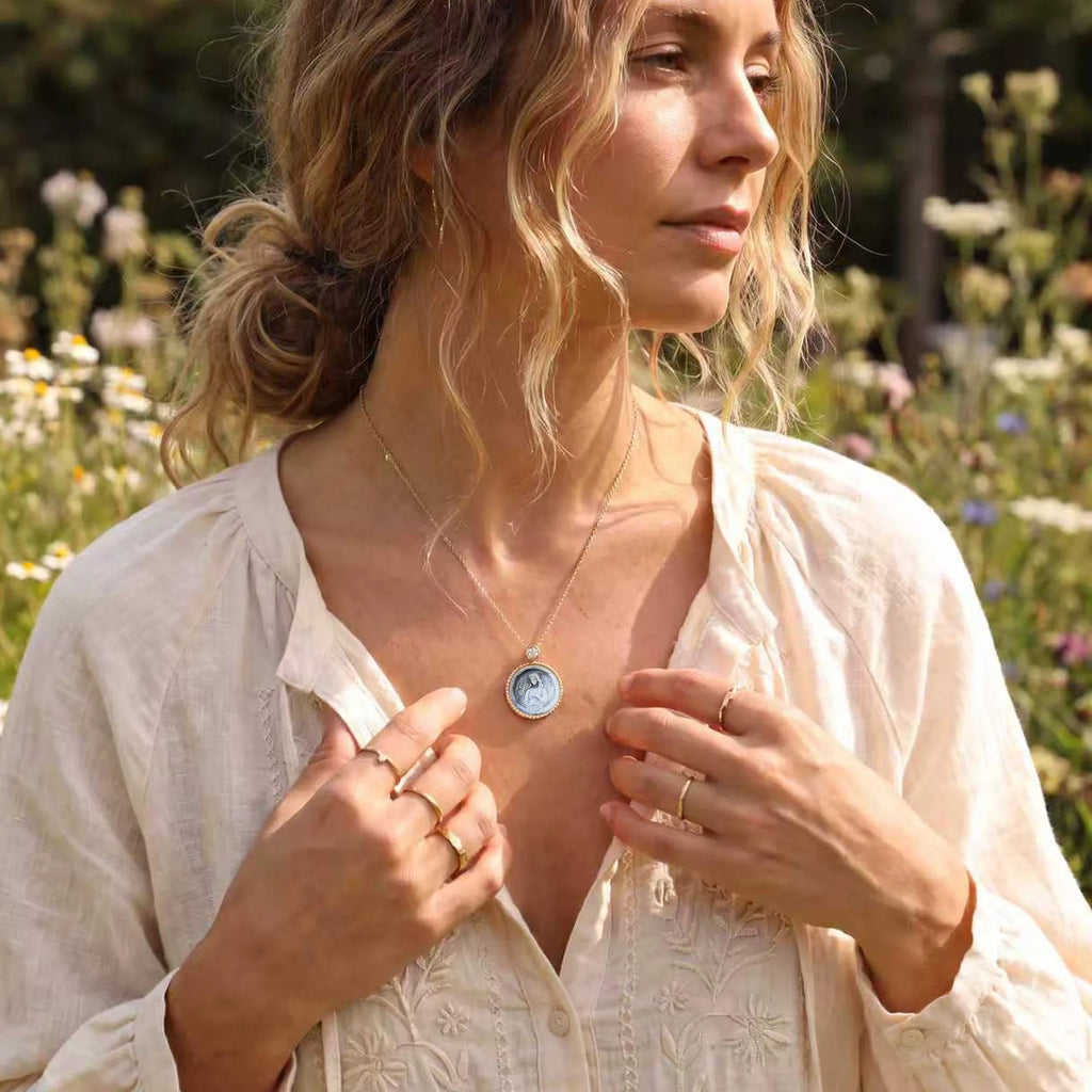 Elegant blonde woman amid countryside wildflowers wearing a Van Gogh style carved  Virgo  zodiac mother‑of‑pearl pendant necklace in gold plated sterling silver by OceanCarvingLab.